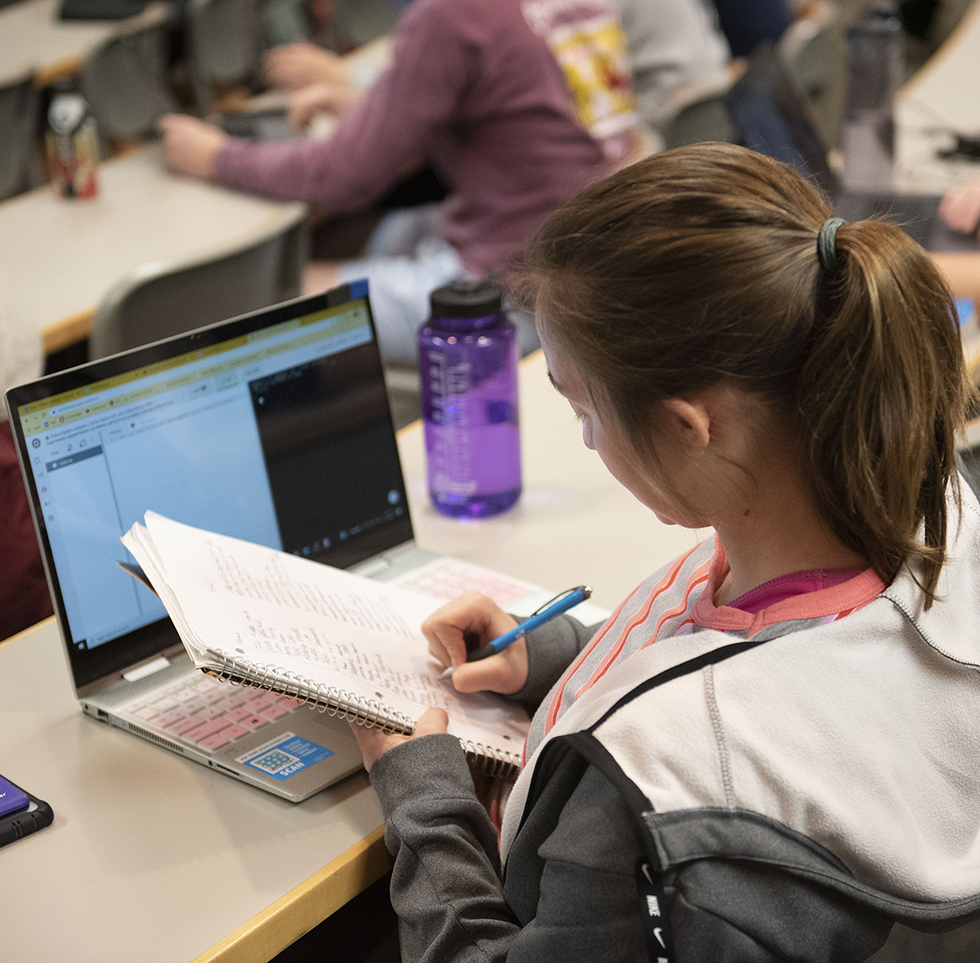 A student takes notes while working at her computer.