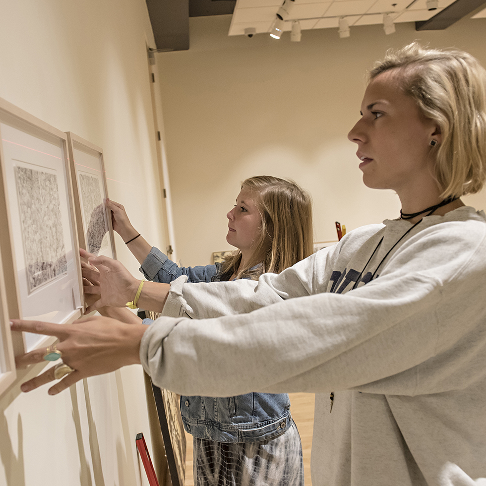 Students hang art for a gallery exhibit/