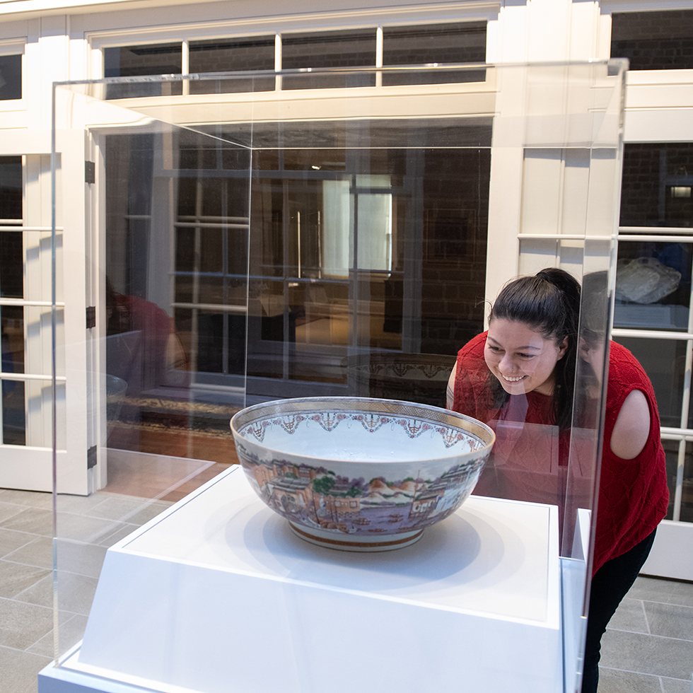 A student examines a piece of Asian pottery in a display case